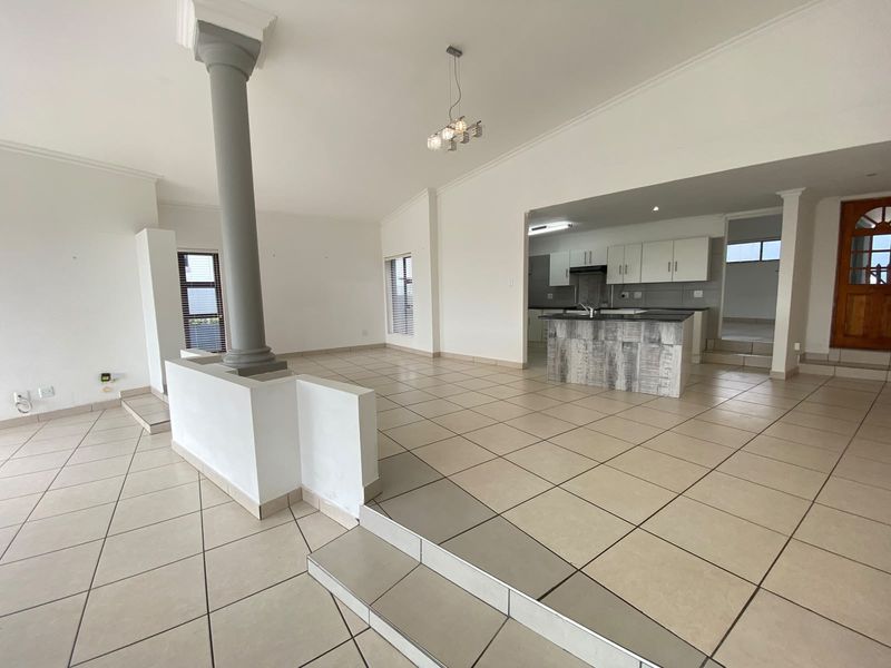 Spacious open-plan living and kitchen area featuring tiled floors, a central kitchen island, and a sunken living room layout with neutral finishes.