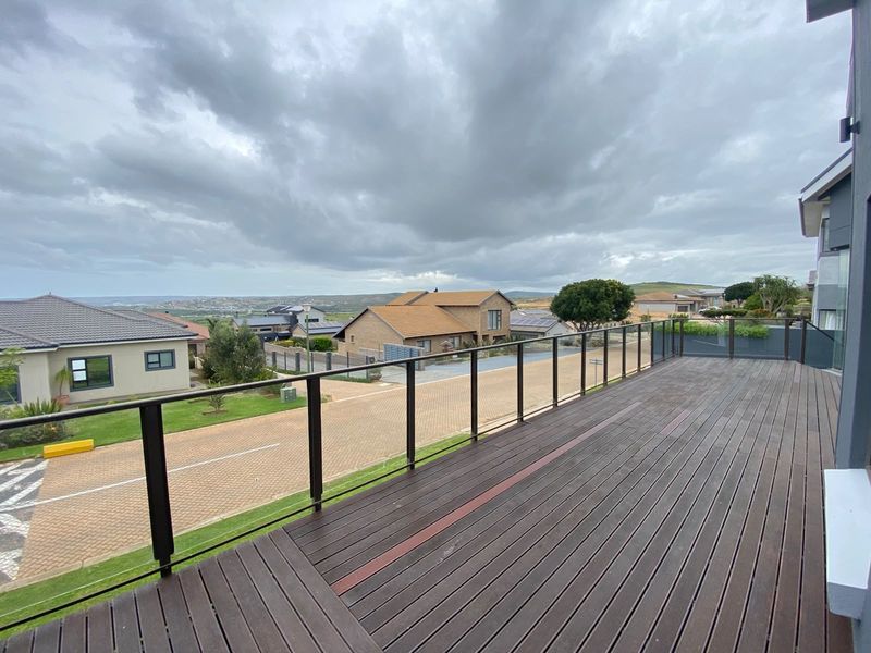 Spacious elevated timber balcony featuring a modern glass balustrade with expansive views over the surrounding residential estate.