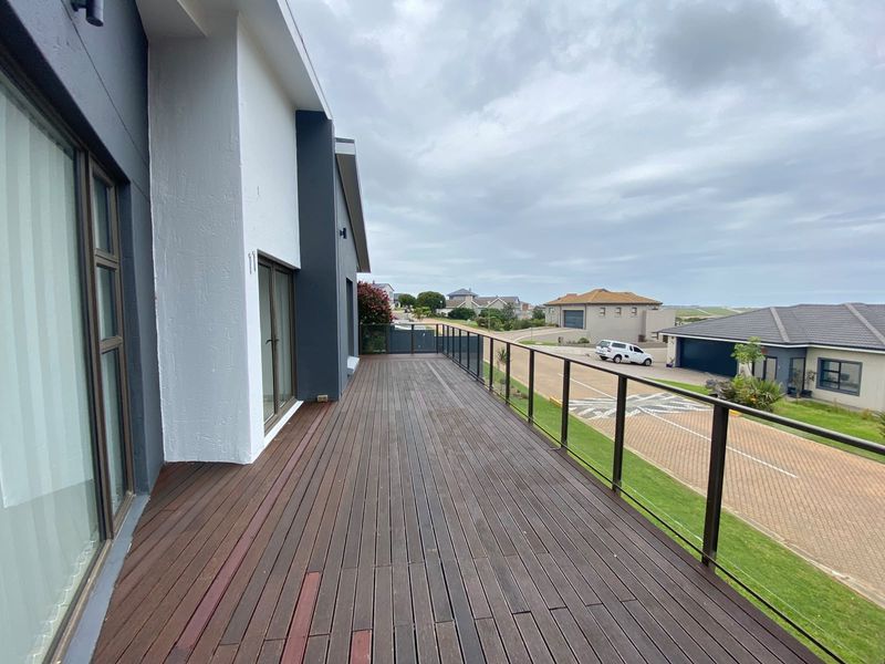 Spacious elevated timber balcony featuring a modern glass balustrade, offering an open outdoor area with views of the surrounding neighborhood.