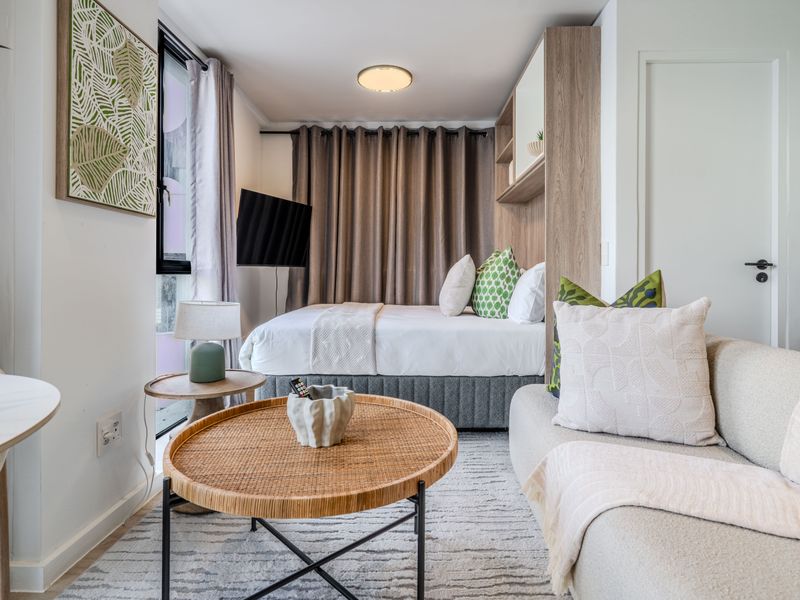 A compact open-plan studio apartment featuring a combined living and sleeping area with integrated shelving and modern finishes.