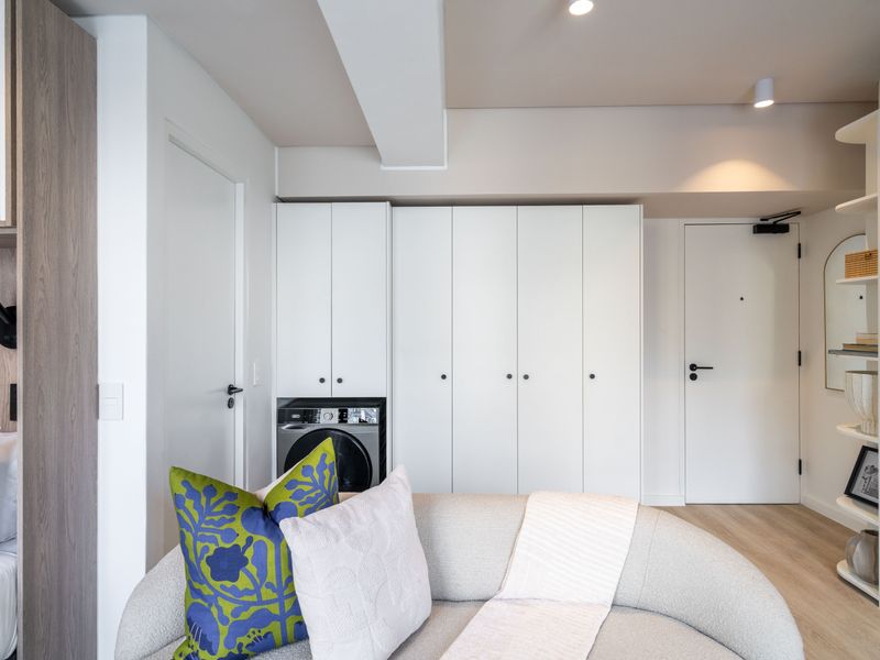 Modern open-plan living area featuring sleek built-in cabinetry with an integrated washing machine, recessed lighting, and light-toned laminate flooring.