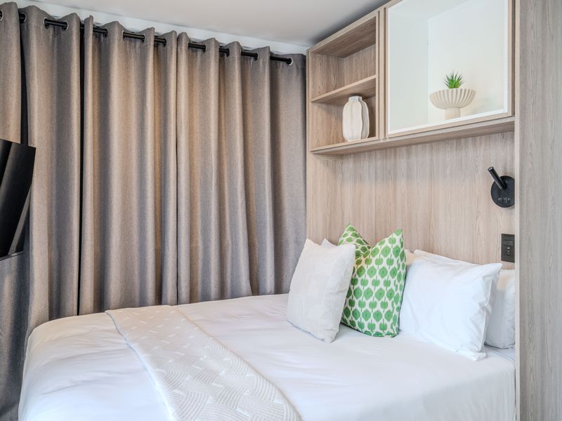 A well-maintained bedroom featuring a modern built-in headboard with integrated shelving and wall-mounted lighting.