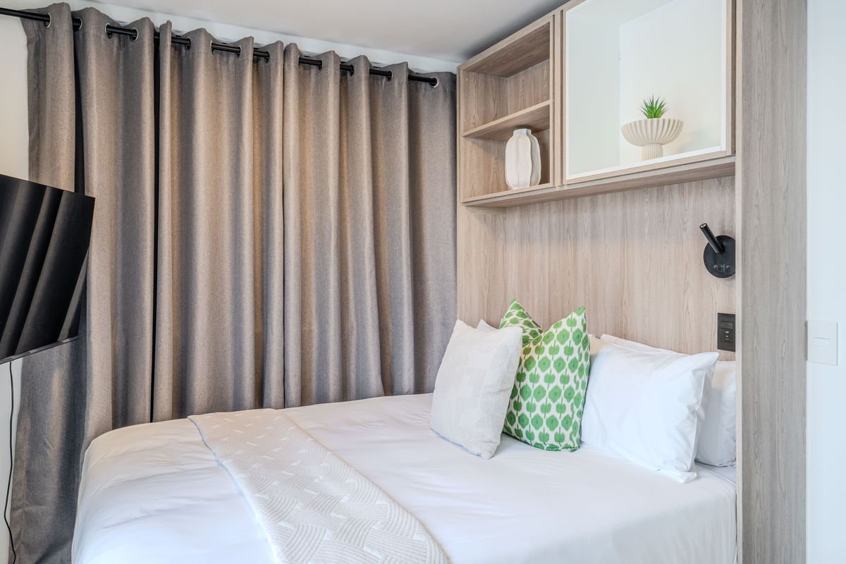 A well-maintained bedroom featuring a modern built-in headboard with integrated shelving and wall-mounted lighting.