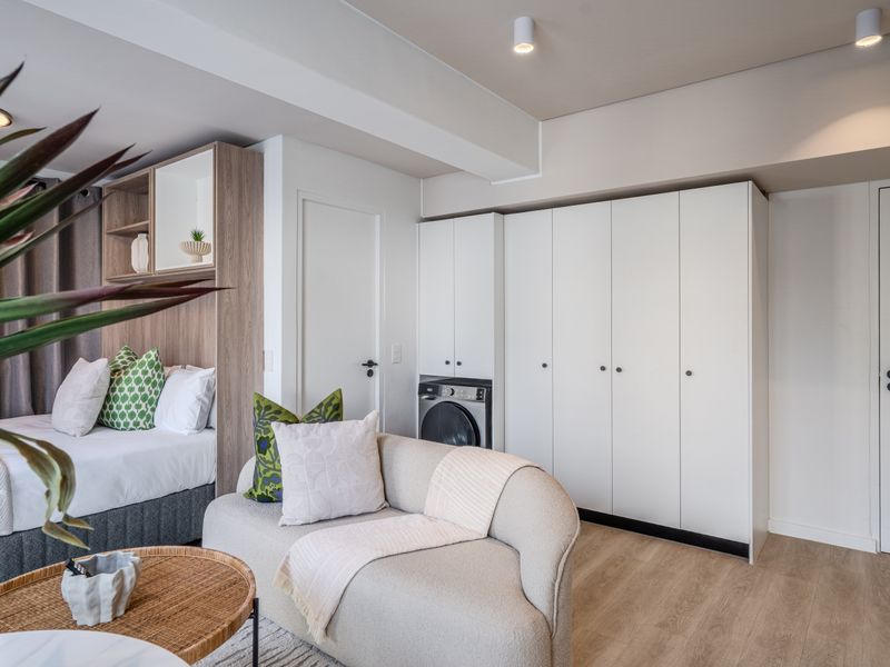 Modern open-plan studio apartment featuring integrated laundry cabinetry, neutral finishes, and recessed ceiling lighting in a well-maintained living and sleeping space.