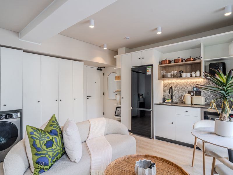 Modern open-plan living area featuring a compact, well-appointed kitchen with integrated appliances, stone countertops, and extensive built-in storage cabinetry.