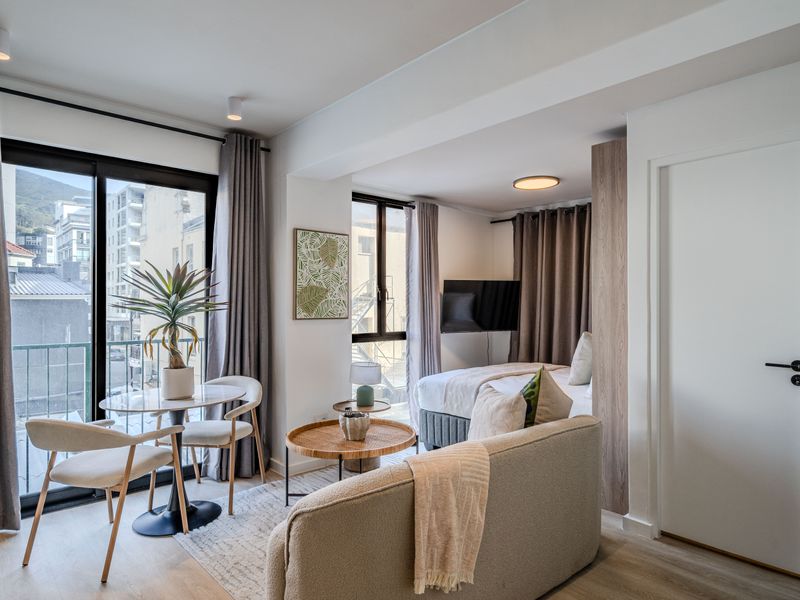 A modern open-plan studio apartment featuring light laminate flooring, recessed lighting, and a sliding glass door leading to a private balcony.