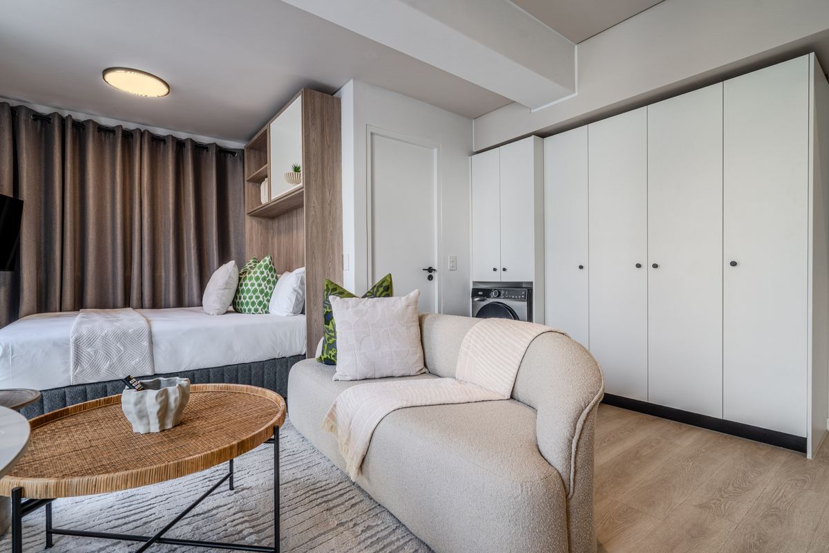 A modern open-plan studio apartment featuring integrated laundry cabinetry, light laminate flooring, and efficient built-in storage solutions.