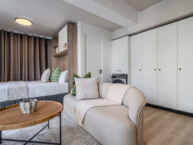 A modern open-plan studio apartment featuring integrated laundry cabinetry, light laminate flooring, and efficient built-in storage solutions.