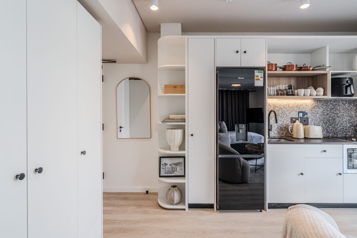 Modern compact kitchen featuring sleek white cabinetry, integrated appliances, stone-look backsplash, and efficient built-in shelving, finished with high-quality laminate flooring and recessed lighting.