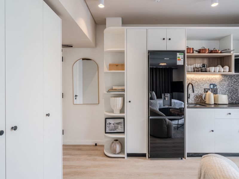 Modern compact kitchen featuring sleek white cabinetry, integrated appliances, stone-look backsplash, and efficient built-in shelving, finished with high-quality laminate flooring and recessed lighting.