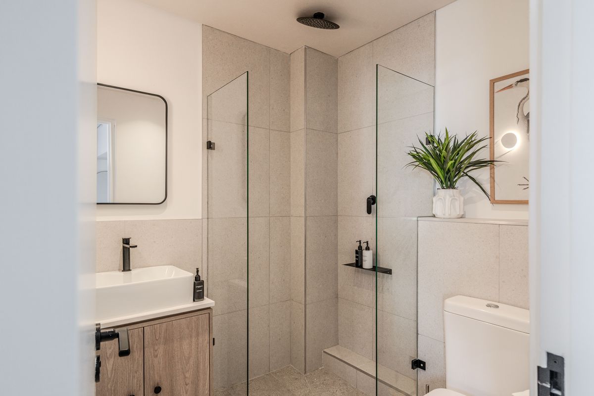 Modern bathroom featuring a walk-in shower with glass screen, rain shower head, vessel sink on a wood-finish vanity, and neutral wall tiling.