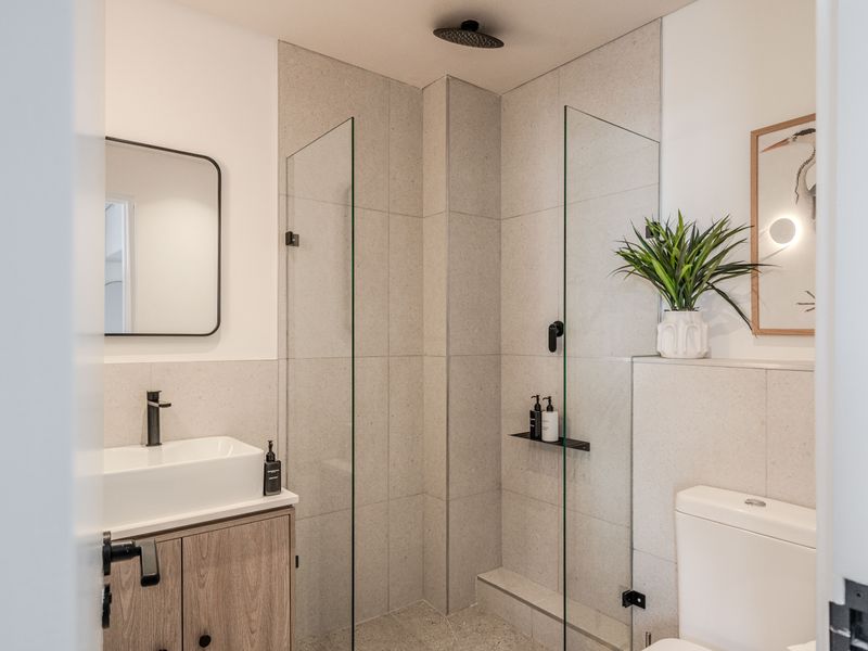 Modern bathroom featuring a walk-in shower with glass screen, rain shower head, vessel sink on a wood-finish vanity, and neutral wall tiling.