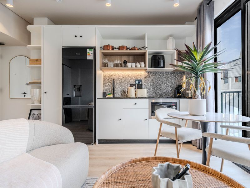 Modern open-plan apartment living area featuring a compact, well-appointed kitchen with sleek cabinetry, stone finishes, and direct access to a private balcony.