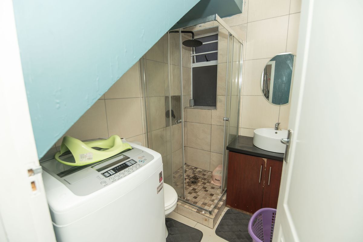 Compact bathroom featuring a shower enclosure, vessel sink with vanity cabinet, and tiled finishes, situated under a sloped ceiling.