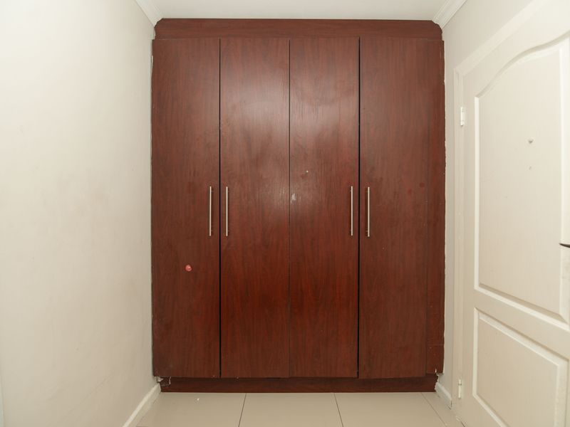 A bedroom featuring a large built-in wooden wardrobe with modern handles and neutral tiled flooring.