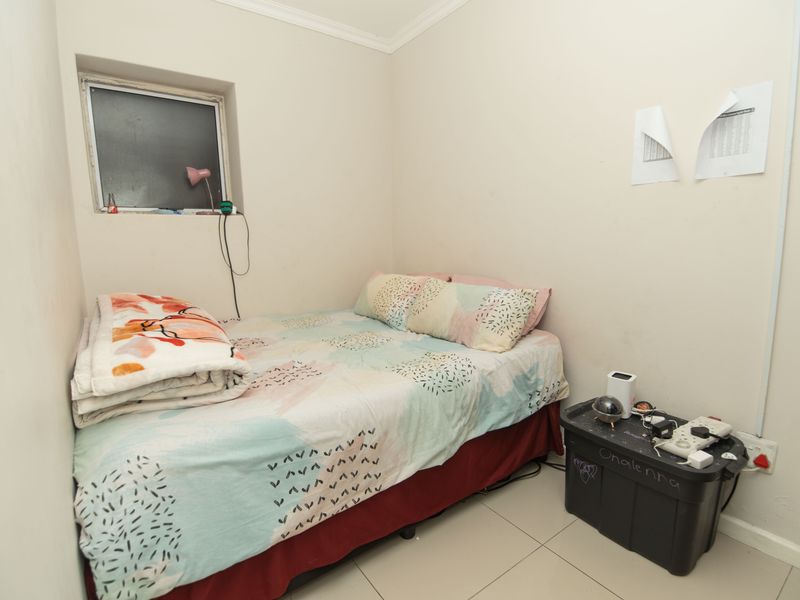 A compact bedroom featuring tiled flooring and a small window, providing a functional space that could benefit from cosmetic updates.