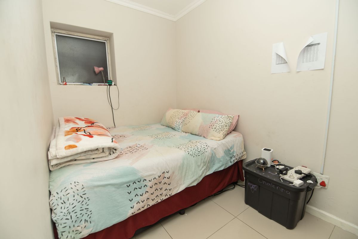 A compact bedroom featuring tiled flooring and a small window, providing a functional space that could benefit from cosmetic updates.