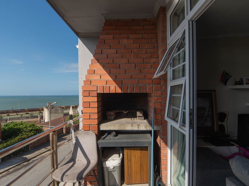A balcony featuring a built-in brick braai, stainless steel balustrade, and expansive coastal views, providing an ideal space for outdoor entertaining.