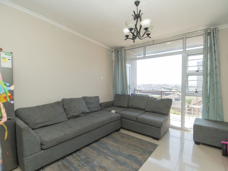 A bright living room featuring tiled flooring, ceiling cornice, and a large aluminium sliding door providing access to a balcony with city views.