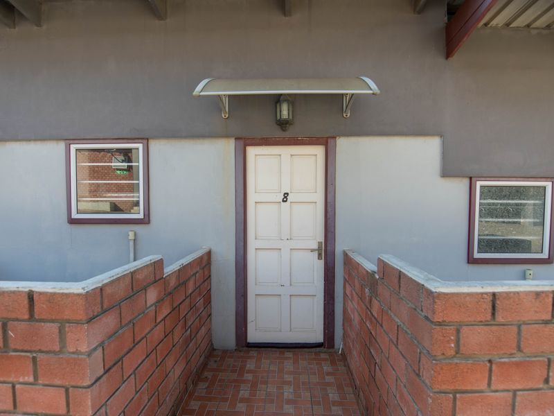 Entrance area featuring a panelled door, brick boundary walls, and a tiled walkway, providing direct access to the apartment unit.