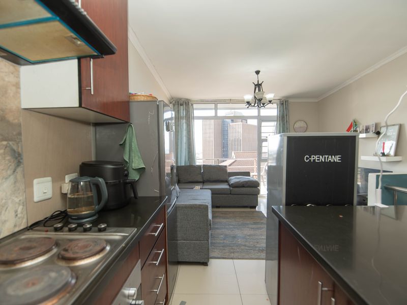 Open-plan kitchen and living area featuring dark cabinetry, stone countertops, electric hob, and direct access to a balcony with city views.