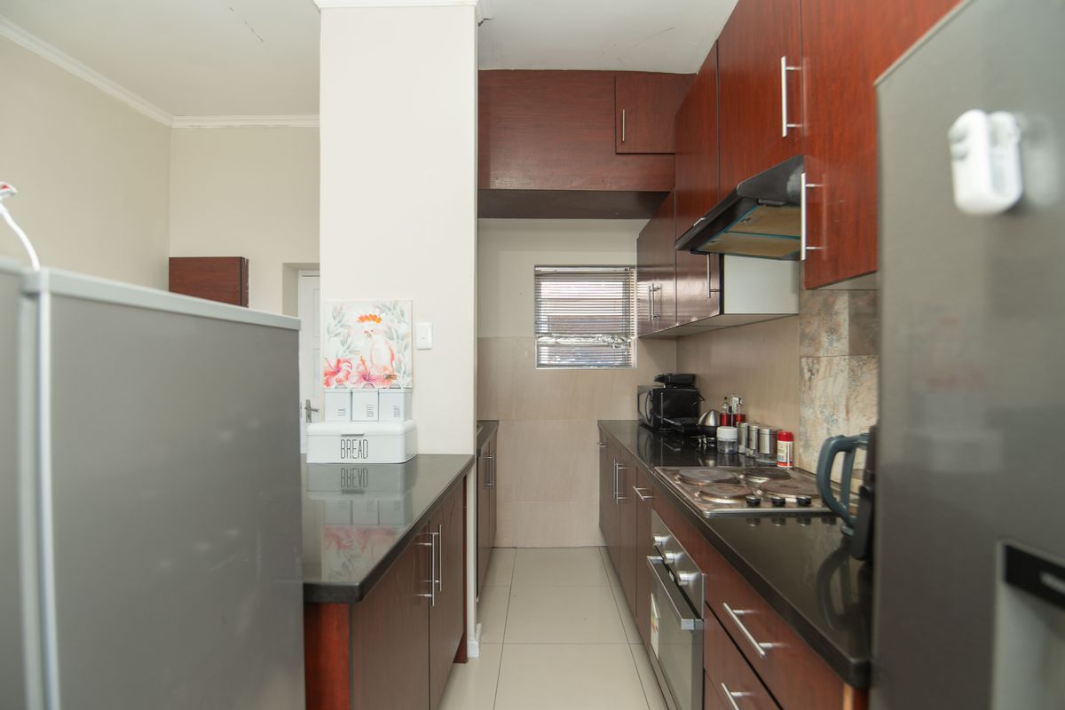 A functional galley-style kitchen featuring dark wood cabinetry, granite countertops, built-in oven, hob, and extractor fan with tiled backsplash and flooring.