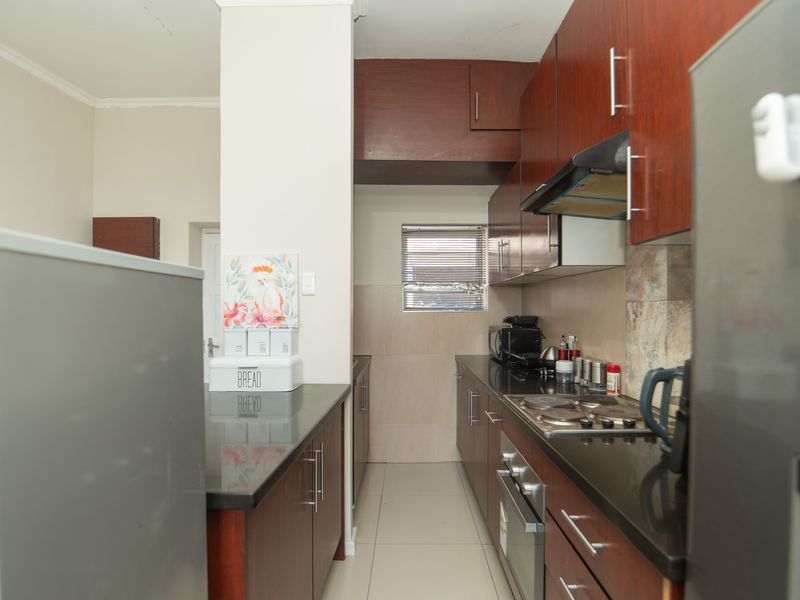 A functional galley-style kitchen featuring dark wood cabinetry, granite countertops, built-in oven, hob, and extractor fan with tiled backsplash and flooring.