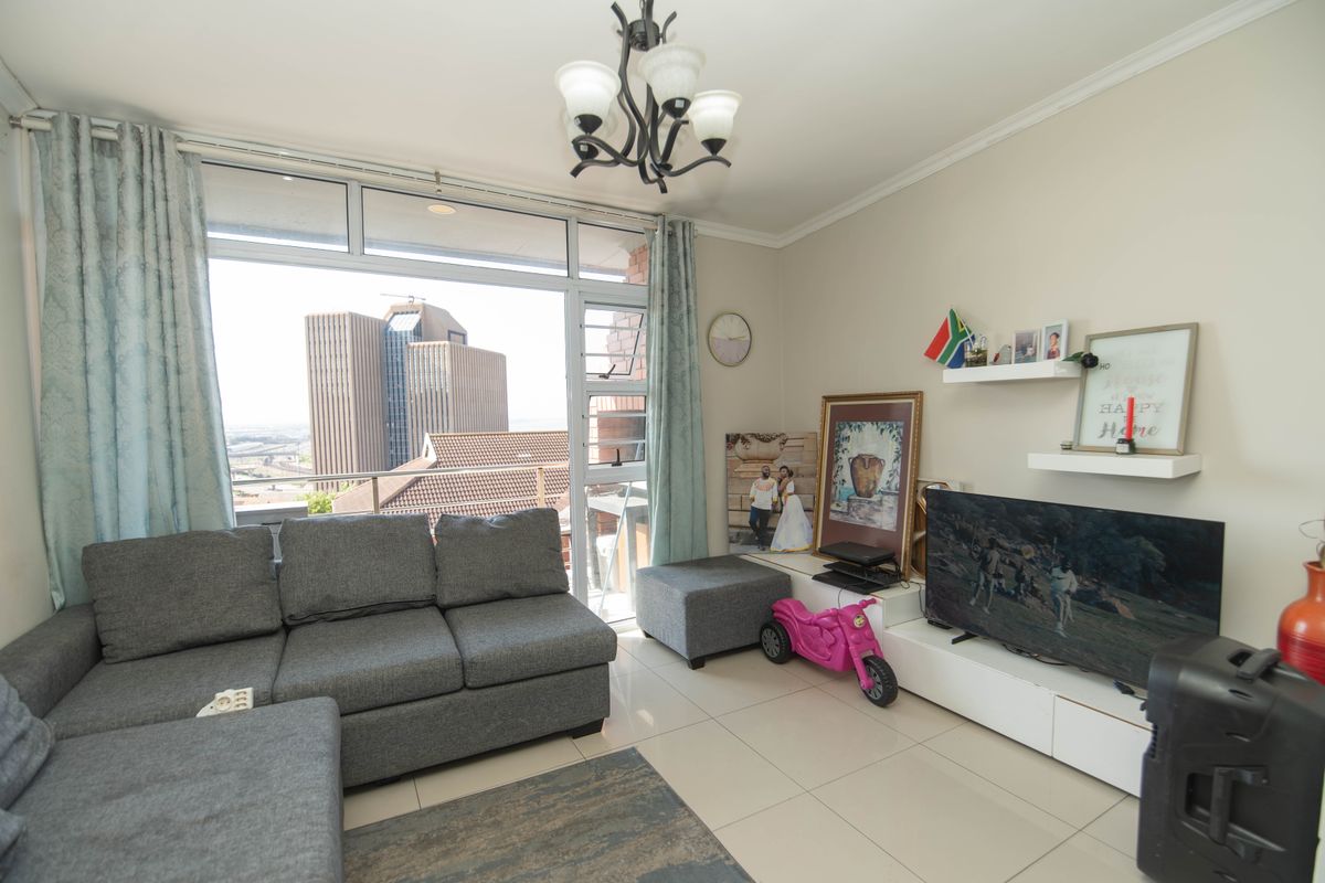 A bright living room featuring large windows with city views, tiled flooring, and a neutral color palette, offering a comfortable and well-lit living space.
