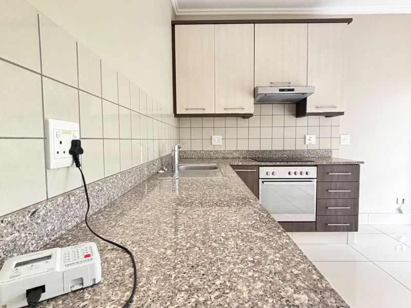 A clean, functional kitchen featuring granite countertops, built-in oven, electric hob, extractor fan, and ample cabinetry with neutral tiled finishes.