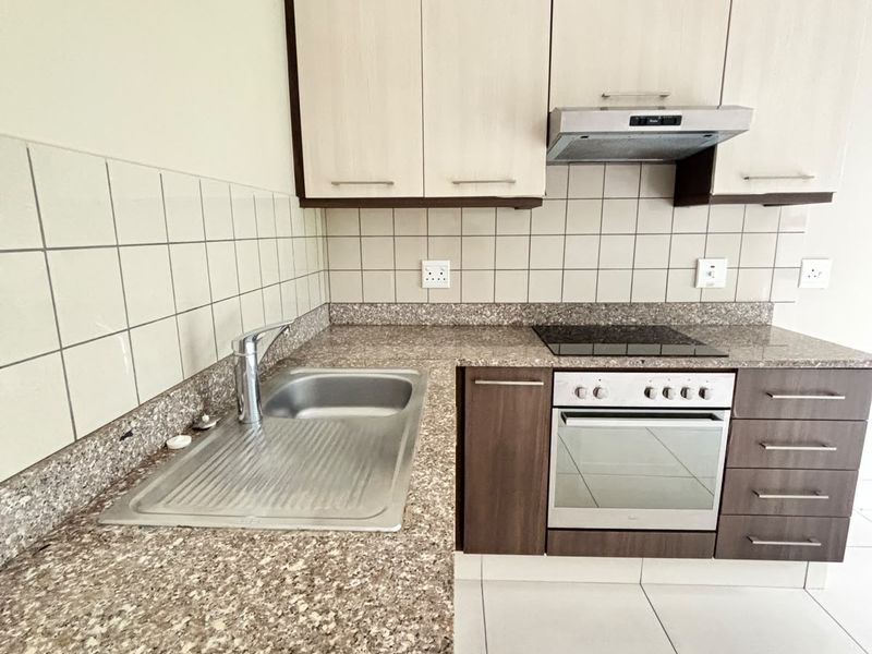 A clean, functional kitchen featuring built-in cabinetry, granite countertops, a stainless steel sink, and integrated electric oven and hob with an extractor fan.