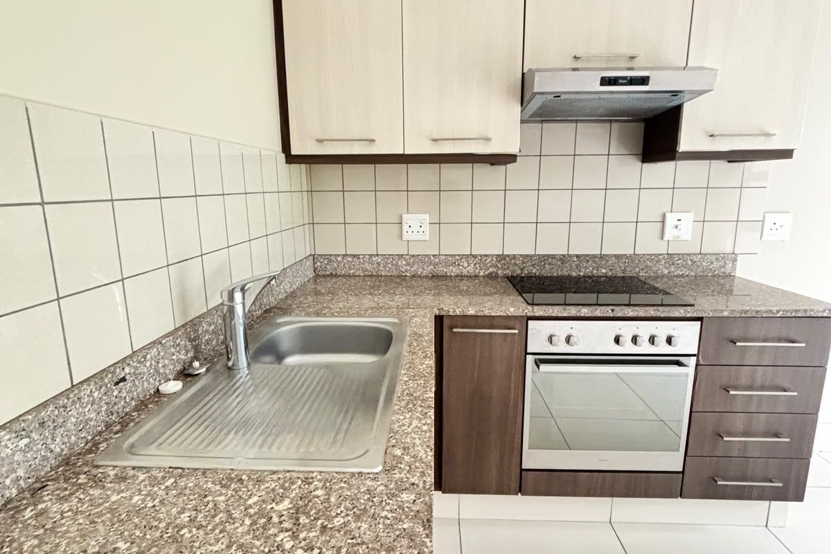 A clean, functional kitchen featuring built-in cabinetry, granite countertops, a stainless steel sink, and integrated electric oven and hob with an extractor fan.