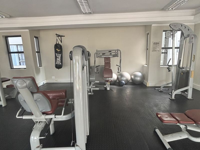 A functional apartment gym facility featuring durable rubber flooring and overhead fluorescent lighting, equipped with various strength training machines.