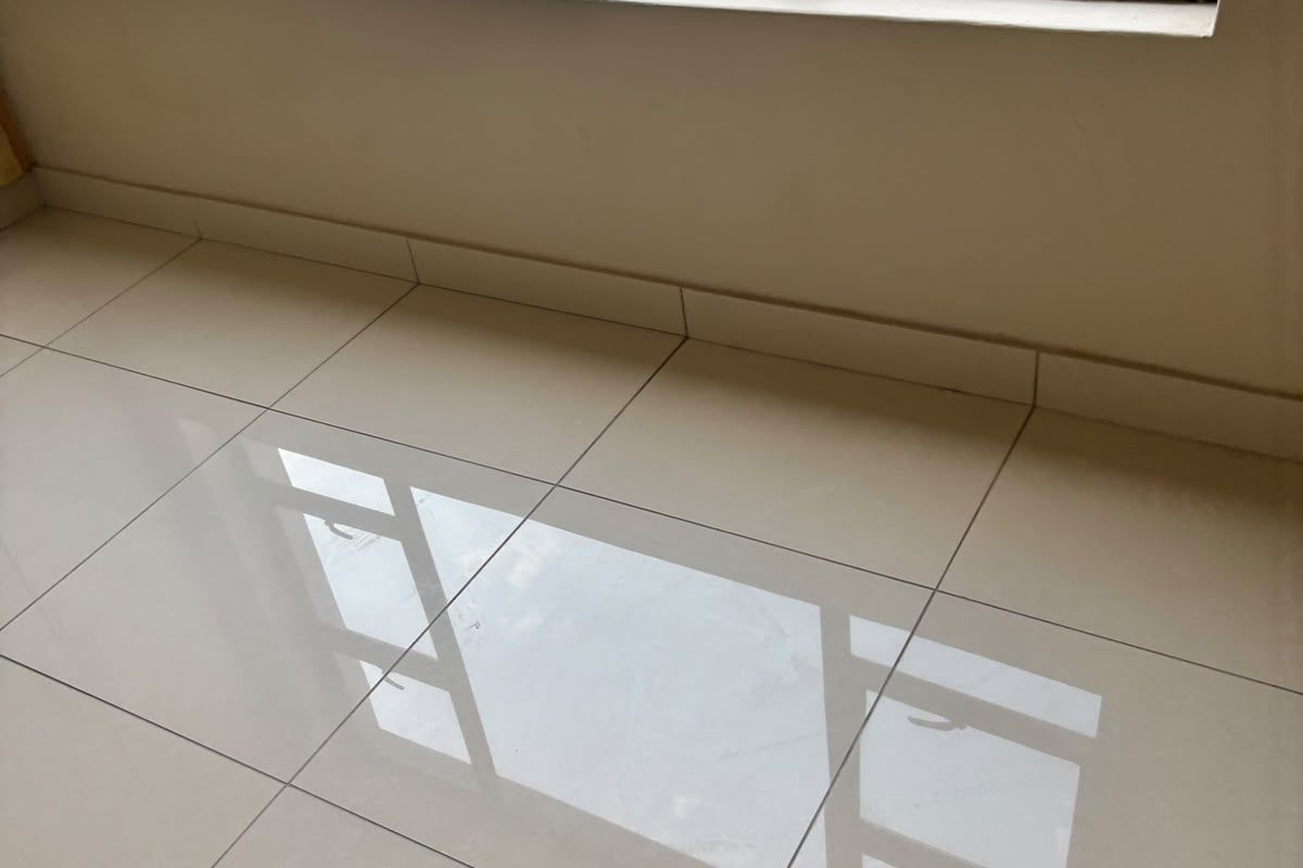 A bright, empty living area featuring large aluminium-framed windows and modern, polished porcelain floor tiles with a clean, neutral finish.