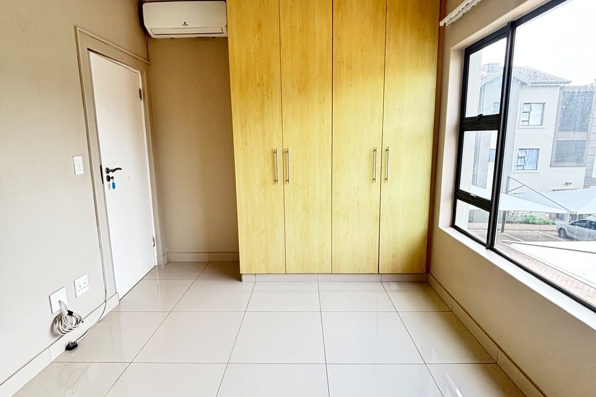 A bright, empty bedroom featuring neutral tiled flooring, built-in wooden cupboards, and a wall-mounted air conditioning unit.