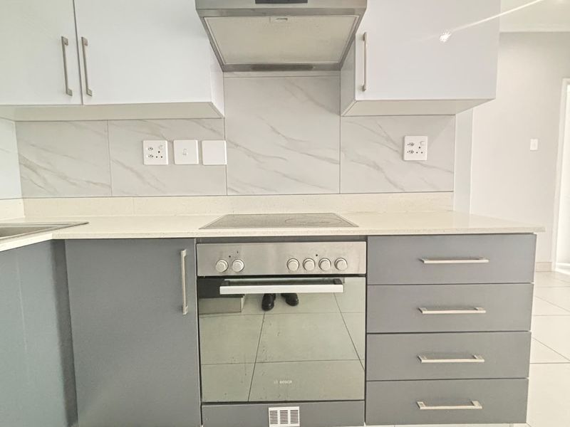 Modern kitchen featuring sleek grey and white cabinetry, quartz countertops, marble-look backsplash, and integrated Bosch oven and hob.