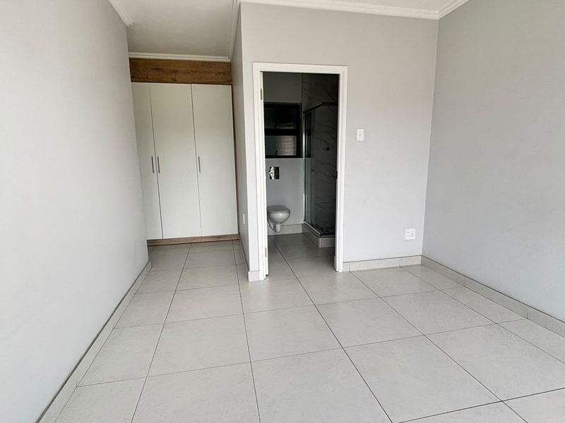 A bright, empty bedroom featuring neutral tiled flooring, built-in cupboards, and direct access to an en-suite bathroom.