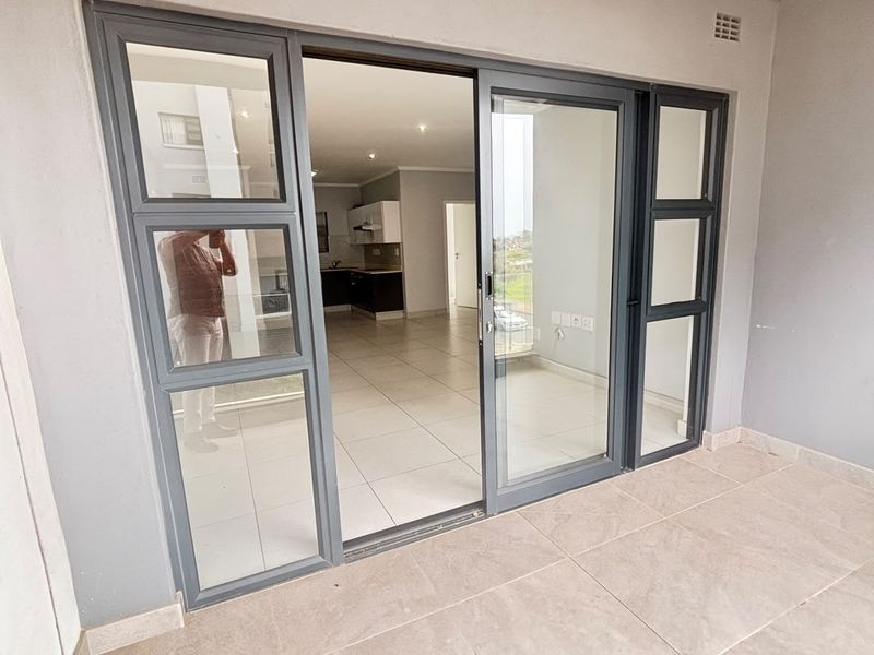 A clean, covered balcony featuring large sliding glass doors that provide access to the interior living space, finished with neutral floor tiles.