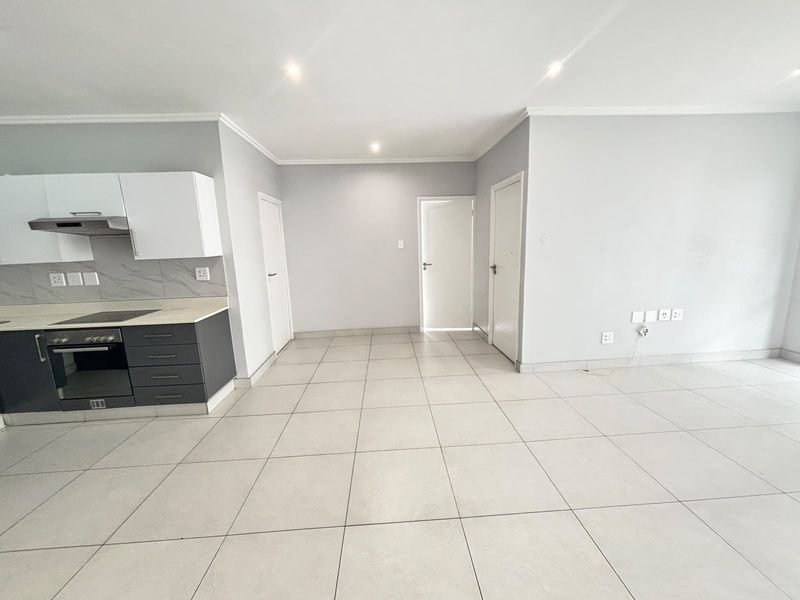 An open-plan living and kitchen area featuring modern tiled flooring, recessed lighting, and a compact kitchen with built-in oven, hob, and extractor fan.