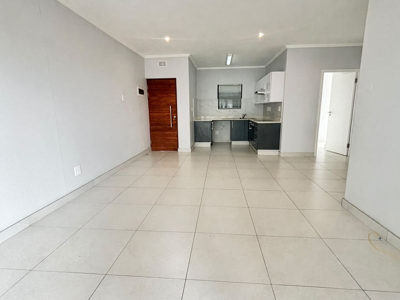 An open-plan living and kitchen area featuring neutral tiled flooring, modern cabinetry, and recessed lighting, offering a clean and versatile space.