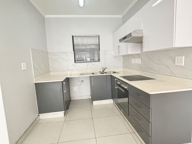 Modern kitchen featuring sleek grey and white cabinetry, stone countertops, marble-look backsplash, and integrated appliances including an electric hob and oven.