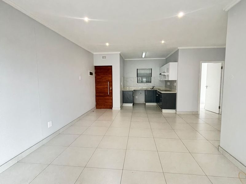 Spacious open-plan living area featuring neutral tiled flooring, recessed lighting, and a functional kitchen with built-in cabinetry.