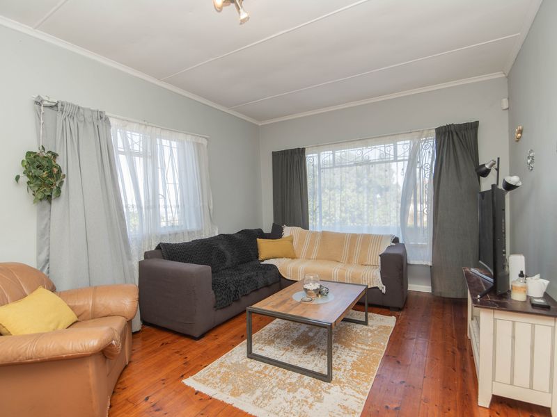 A cozy living room featuring original hardwood flooring and large windows fitted with security bars, offering a bright and functional living space.