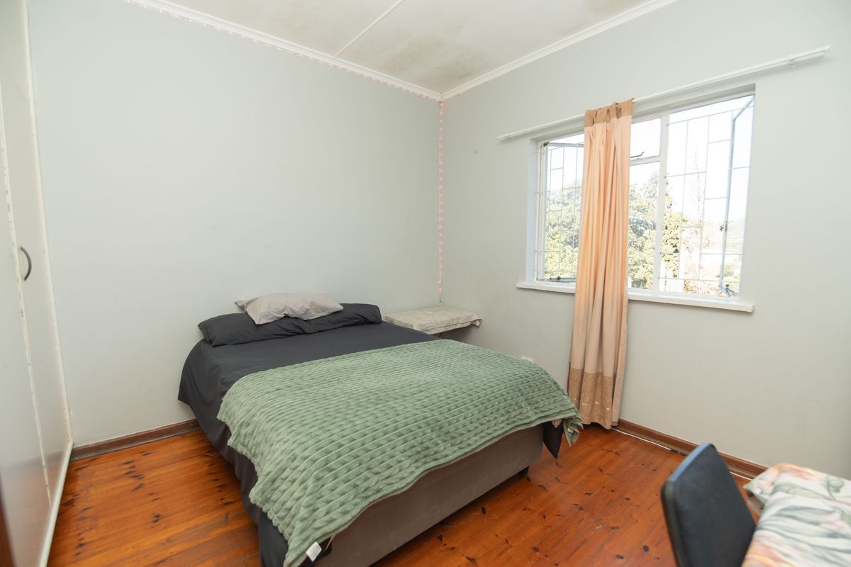 A bedroom featuring timber flooring, a built-in wardrobe, and a window with security bars. The room requires minor cosmetic updates to the ceiling and flooring.