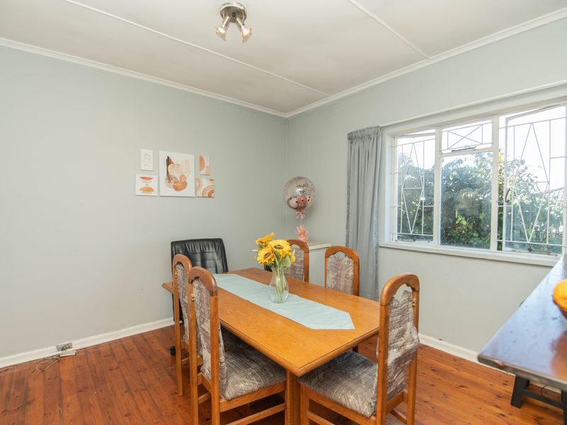 A dining room featuring polished timber flooring, a large window with security bars, and neutral wall tones.