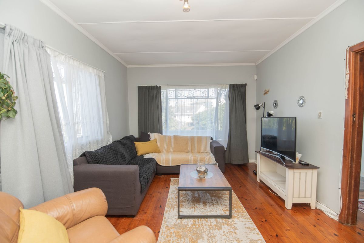 A comfortable living room featuring original hardwood flooring, coved ceilings, and large windows with security bars, offering a bright and functional living space.