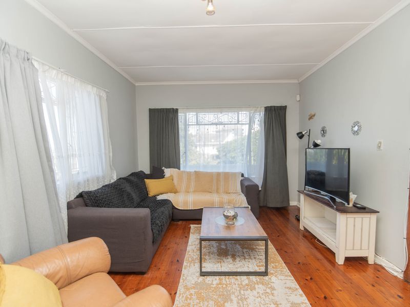 A comfortable living room featuring original hardwood flooring, coved ceilings, and large windows with security bars, offering a bright and functional living space.