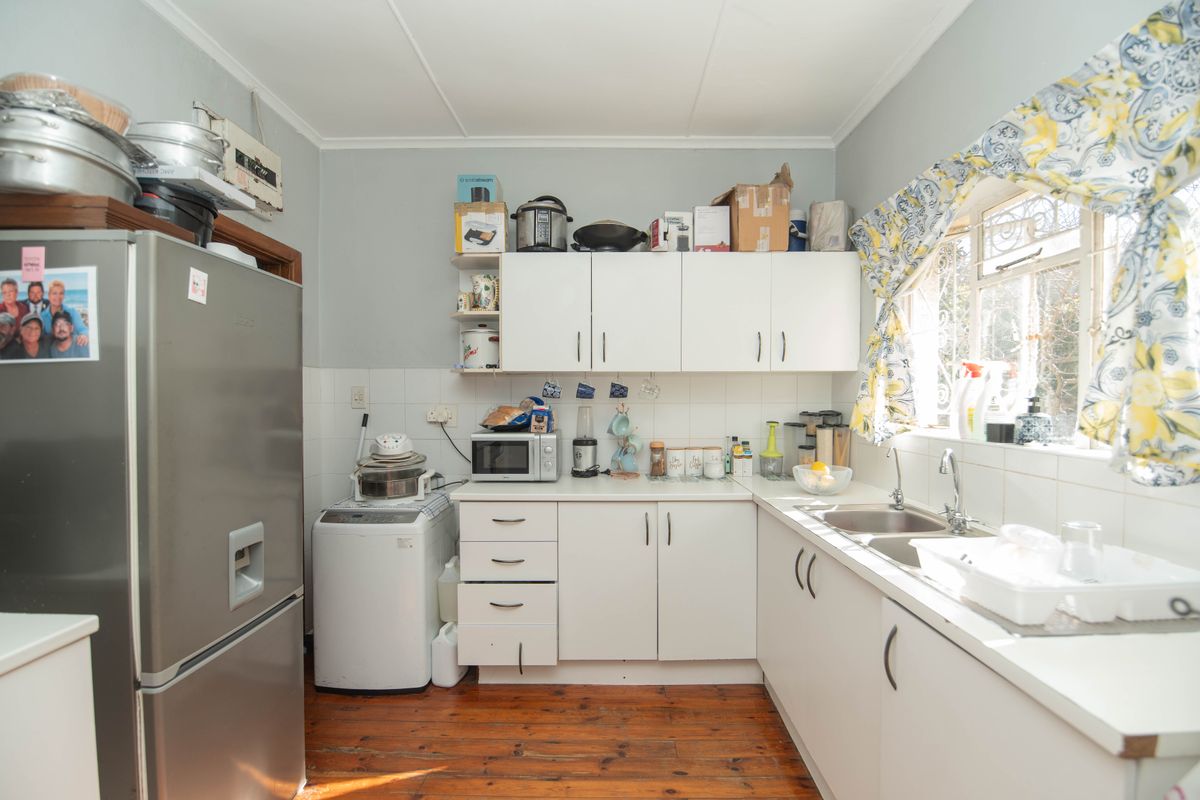 A functional kitchen featuring white cabinetry, a double stainless steel sink, tiled backsplash, and timber flooring, offering a practical layout for daily use.