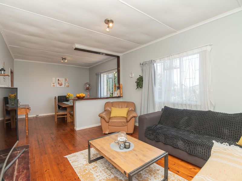 Open-plan living and dining area featuring hardwood flooring, a pass-through kitchen counter, and large windows with security bars.