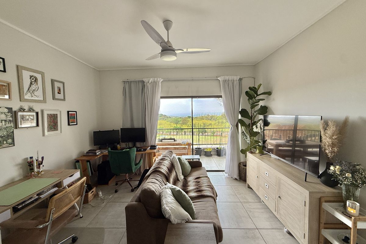 A bright living room featuring tiled flooring, a ceiling fan, and large sliding glass doors that provide natural light and access to a balcony.