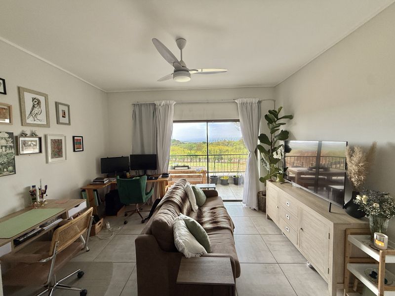 A bright living room featuring tiled flooring, a ceiling fan, and large sliding glass doors that provide natural light and access to a balcony.
